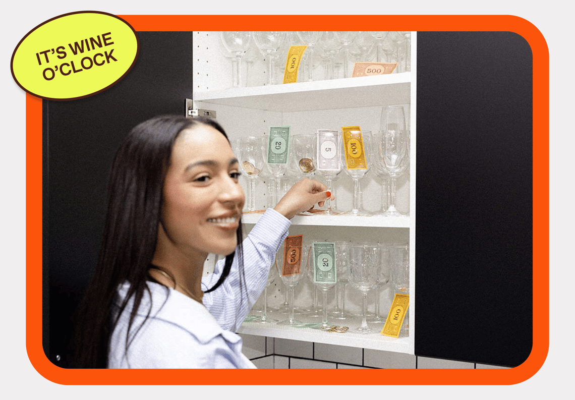 A woman smiling while grabbing a champagne glass filled with money with a sticker that reads 